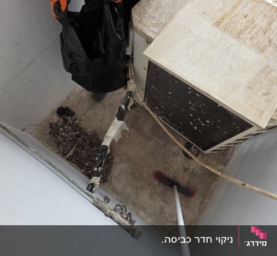אדם עם כפפות כתומות מנקה אזור עם מטאטא ושקית שחורה